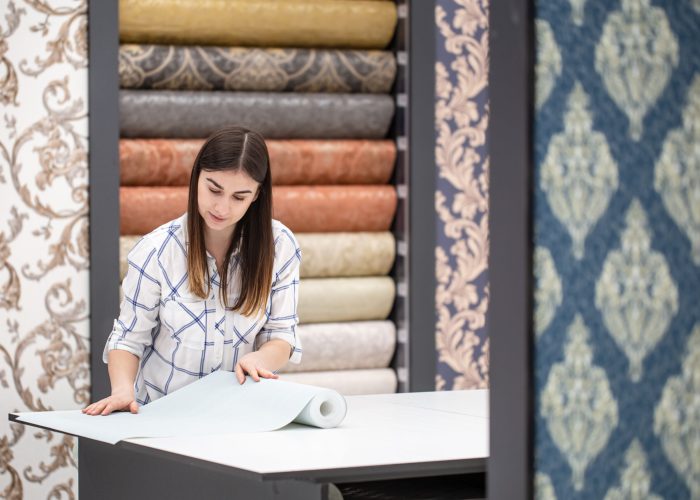 a young woman in a store chooses wallpaper for her home.